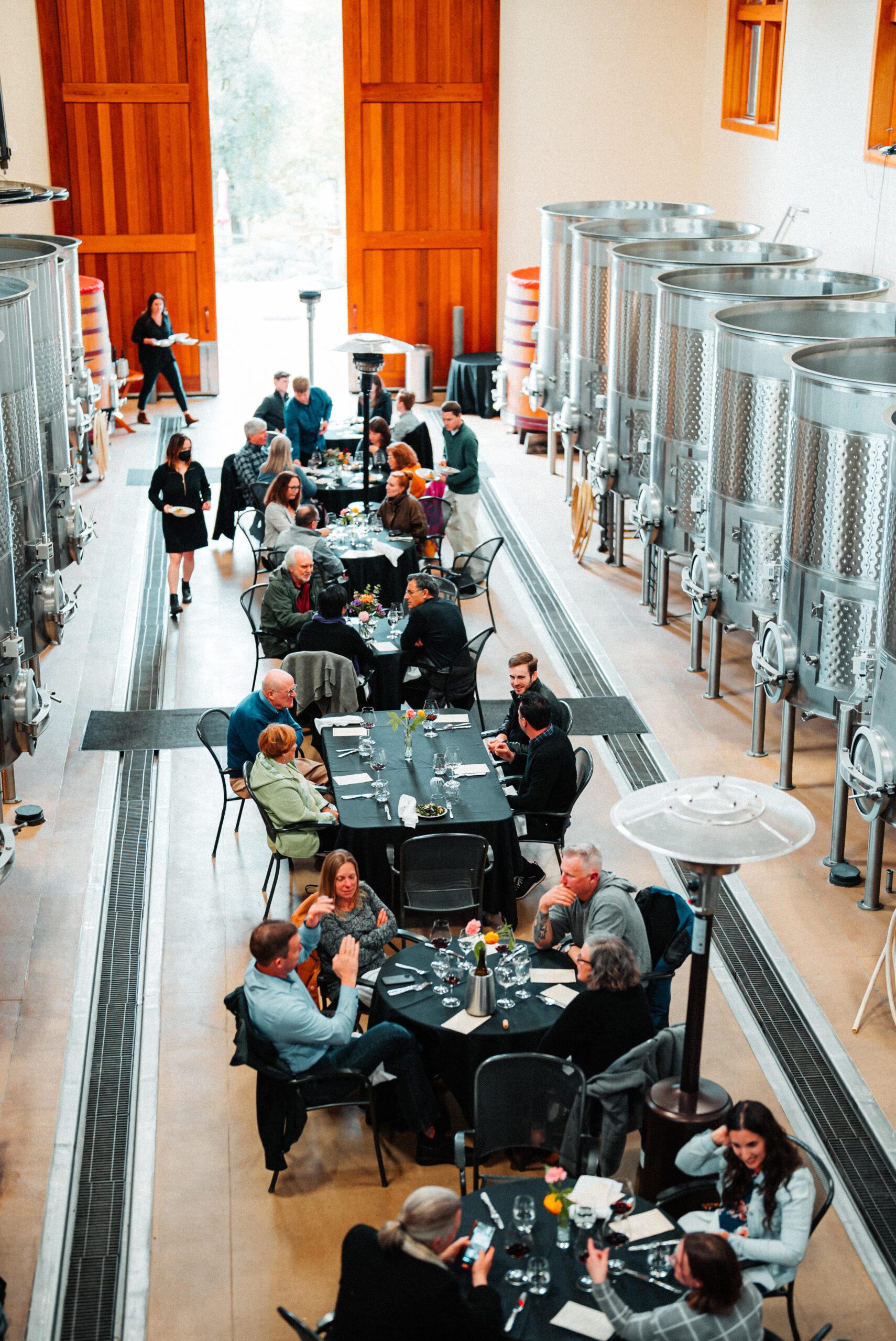 Tables full of people enjoying wine in the steel barrel room